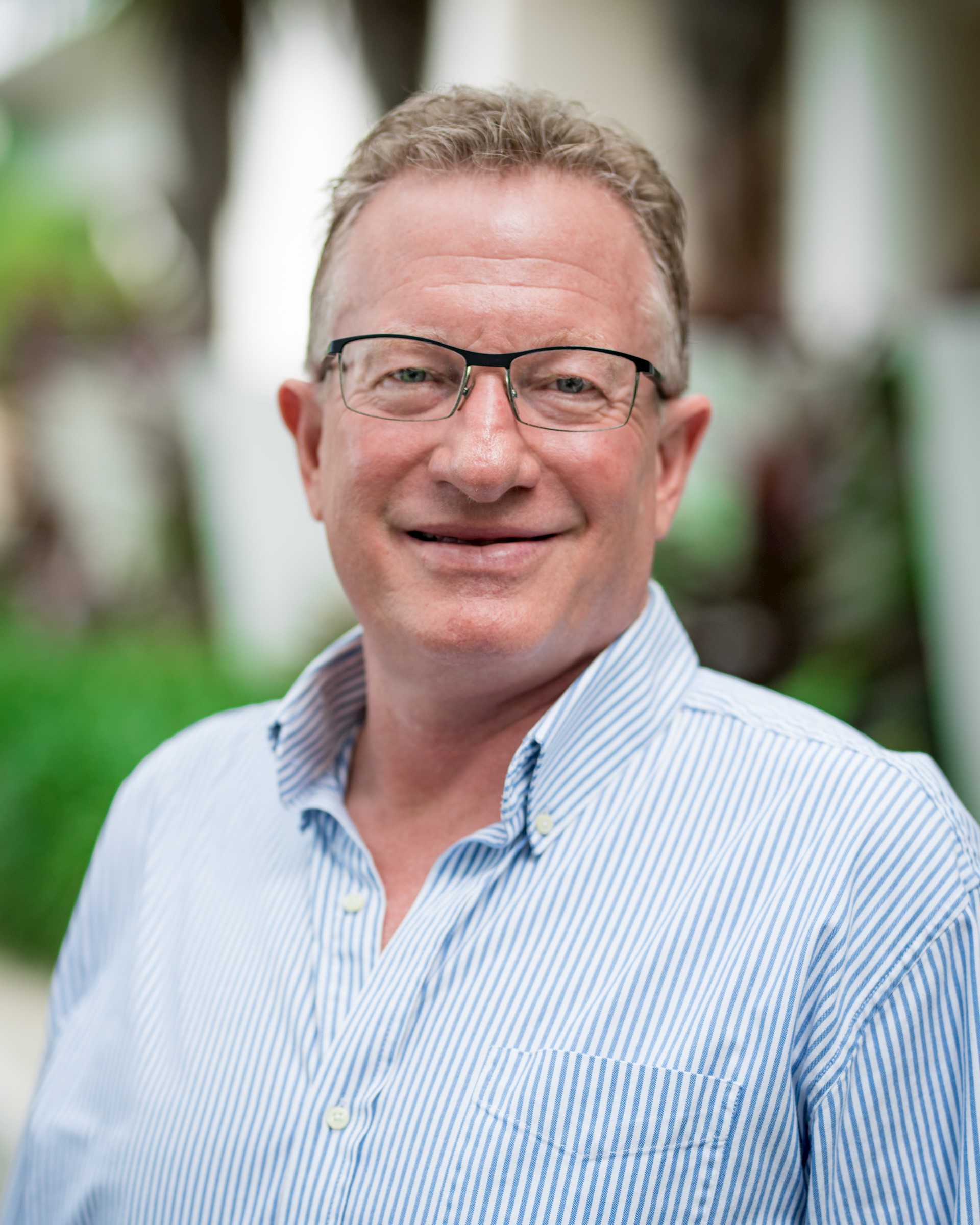 Caucasian man with salt and pepper hair and horn rimmed glasses smiles at the camera