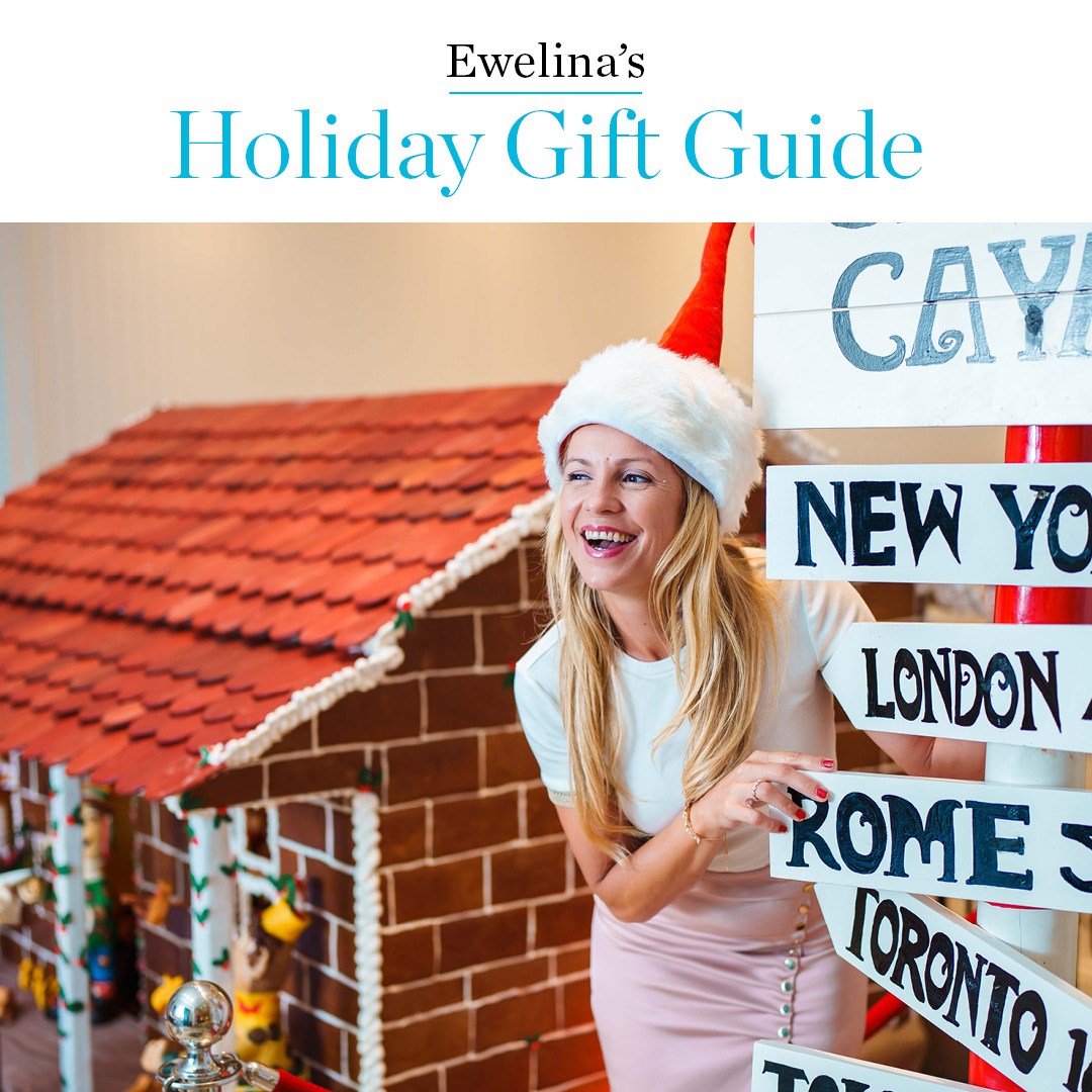 White woman in Christmas hat smiles in front of gingerbread house